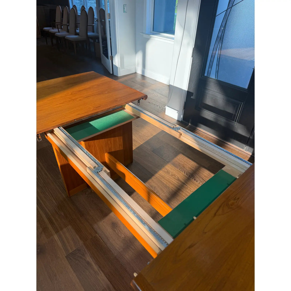Teak expanding dining table, open table showing internal leaf-storage space and rails